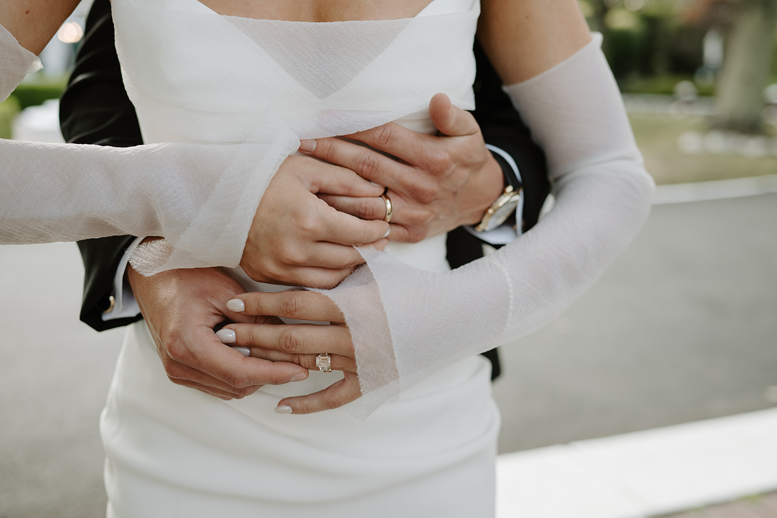 Close-up of the groom's hands wrapped around the bride's waist, showing their elegant wedding rings.